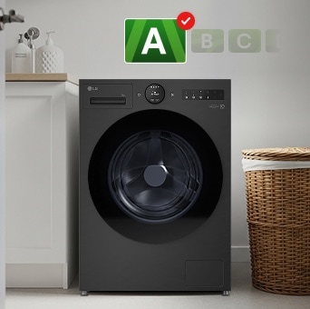 A black LG washing machine with an A energy efficiency label is placed in a laundry room. A brown laundry basket is positioned next to the machine.