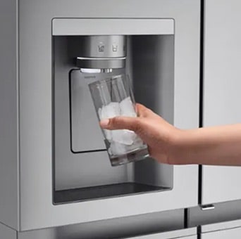 A hand fills a glass with ice cubes from the built-in dispenser of an LG fridge freezer. Ice is coming out of the dispenser located on the front of the refrigerator door.