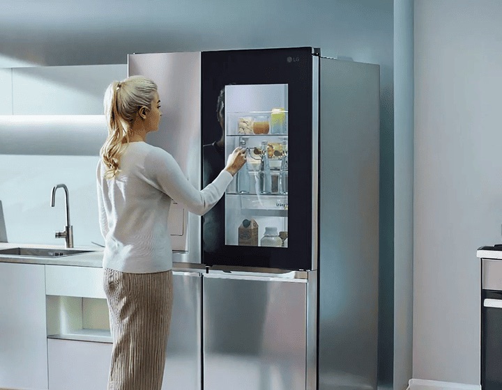 Woman knocks twice on the LG InstaView refrigerator. The glass panel lights up to reveal water bottles inside. She then opens the door and takes one out.