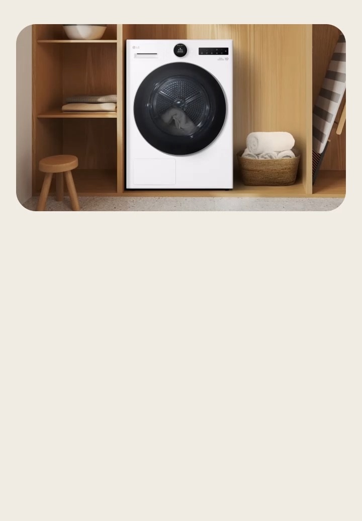 LG white tumble dryer placed in wooden utility shelving with towels and a laundry stool. AI DD sensor detects fabric type and dries towels to a soft finish.