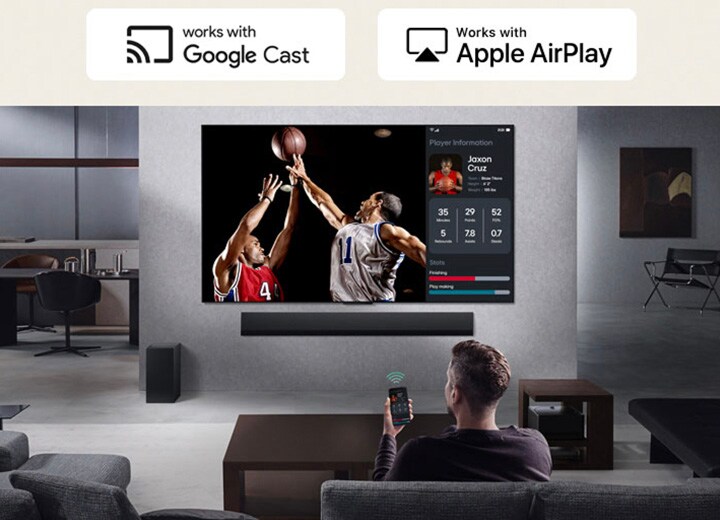 Person im Wohnzimmer, die ein Telefon in der Hand hält. Auf dem Telefon zeigt ein Übertragungssymbol an, dass der Bildschirm des Telefons auf dem Fernseher gespiegelt wird. Im Fernsehen läuft ein Basketballspiel, daneben zeigt ein Spiegelbildschirm Spielerstatistiken an.