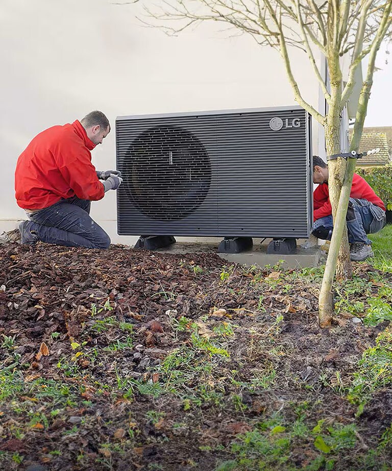 Zwei Installateure mit roter Jacke  installieren die LG Luft/Wasser Wärmepumpe THERMA V R290 Monobloc in einem Garten 