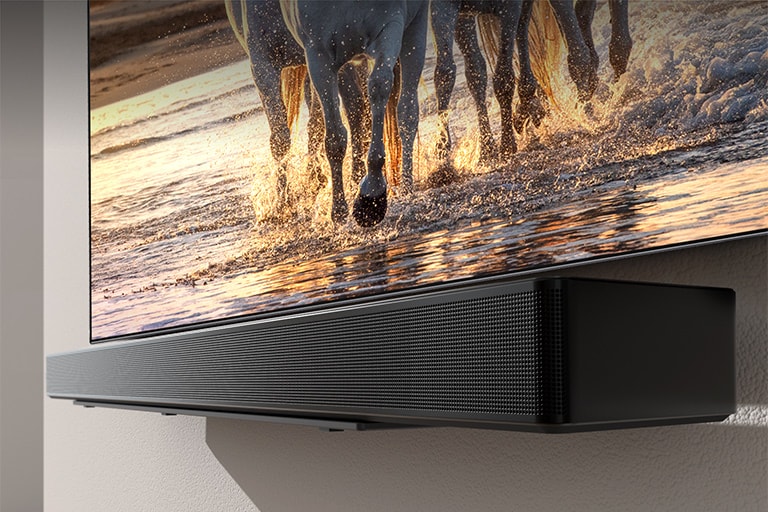 Ein Fernseher, der Pferde zeigt, das bei Sonnenuntergang über einen Strand galoppieren, ist zusammen mit einer Soundbar an einer Wand angebracht.