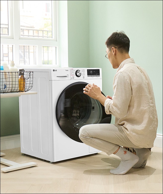 A Mann ladet Wäsche in a Waschmaschine und stellt dabei de Einstellungen ei.