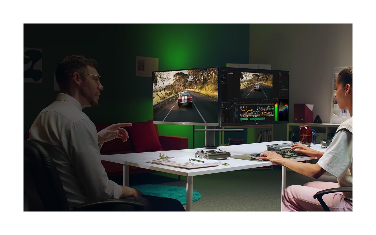 Two people sit at a desk with their own individual monitors. These monitors are connected on one side, creating the impression of a dual monitor.