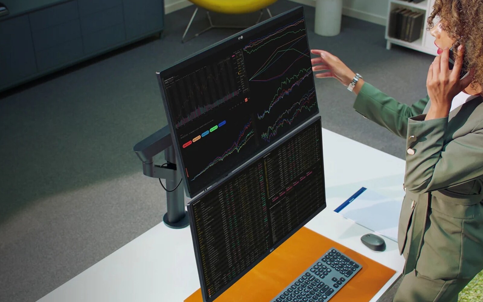 A woman focused on her work, using dual monitors in a well-lit office environment.