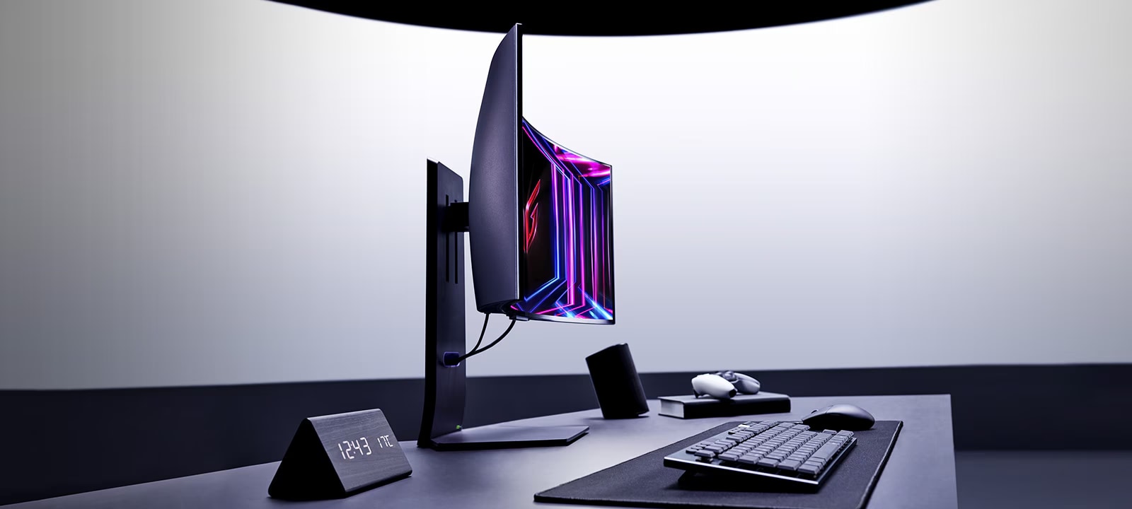 A modern desktop setup features a LG Curved Gaming Monitor with vibrant colours, a keyboard, a mouse, and an angled clock displaying the time. The setup is minimalistic and professional.