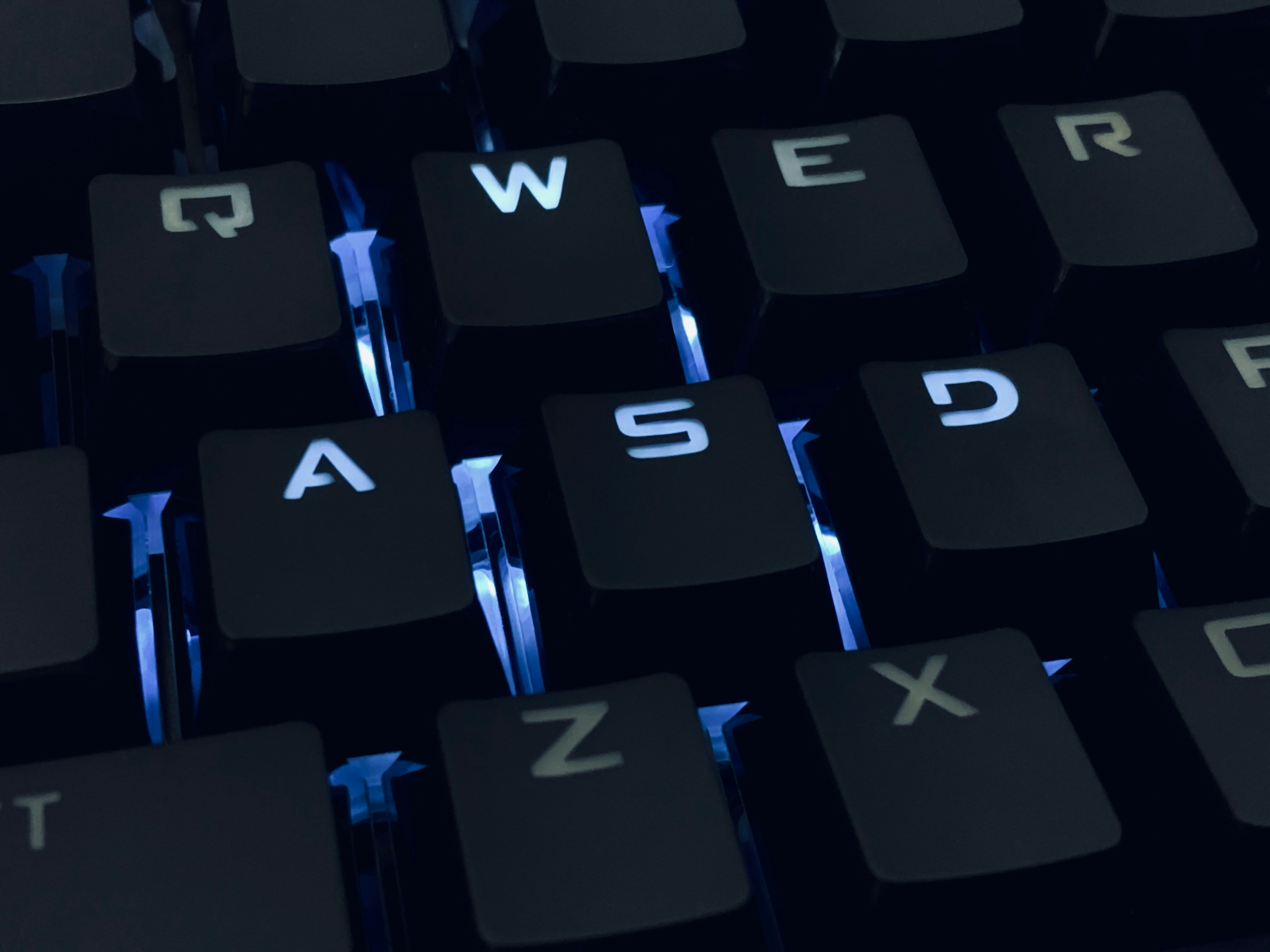 Close-up of a backlit keyboard with a focus on the keys Q, W, E, R, A, S, D, F, Z, and X illuminated in blue.