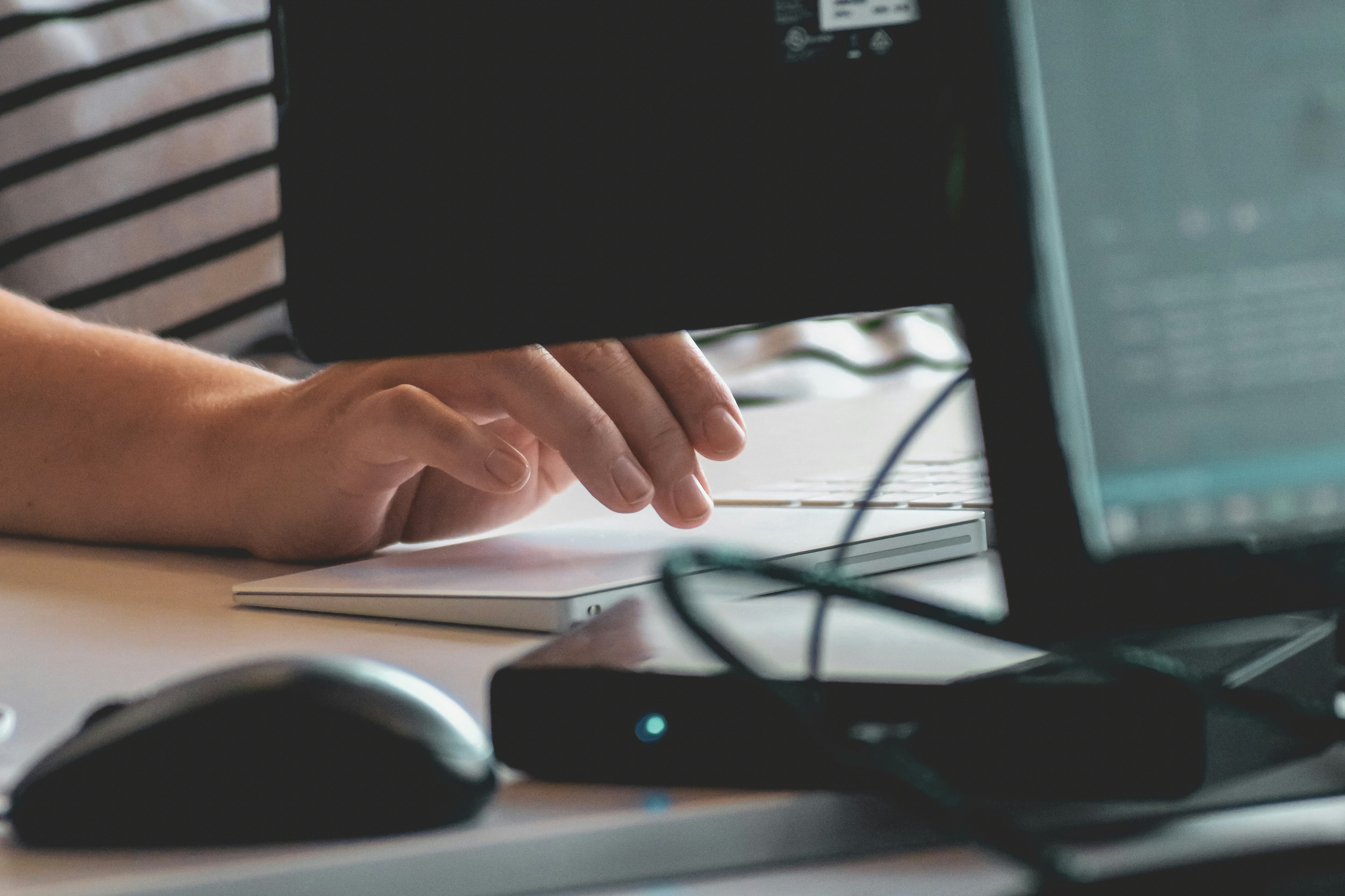 Close-up of a person's hand pointing at a computer screen, with a blurry background showing a keyboard and another monitor.