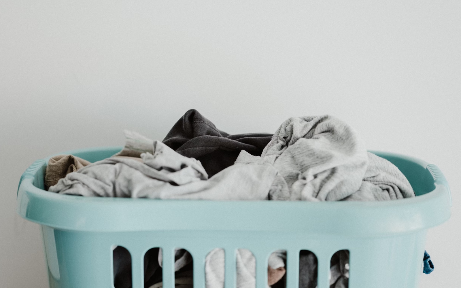 : A light blue laundry basket filled with assorted clothes against a plain white background.