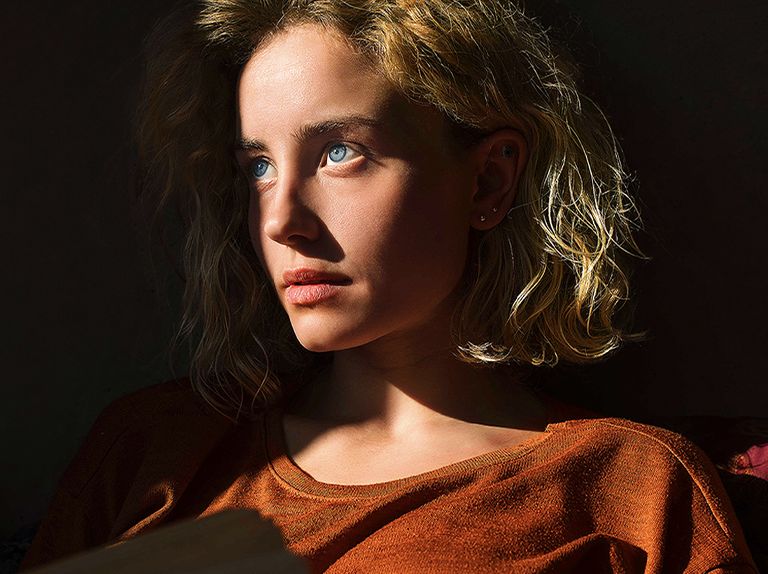 An video of a woman with piercing blue eyes and a burnt orange top in a dark space. Red lines depicting AI refinements cover part of her face, which is bright and detailed, while the rest of the image looks dull.