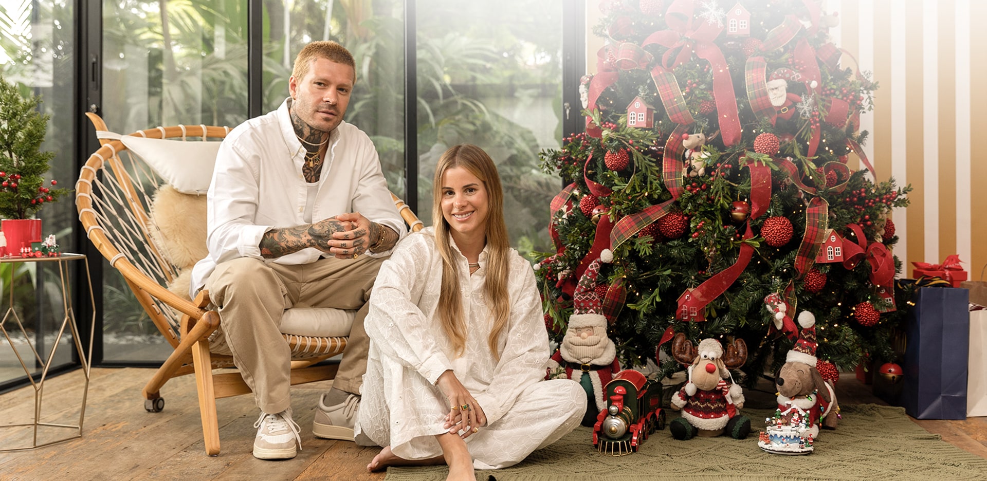 Membros da família sorriem sentados ao lado de uma árvore de Natal decorada em clima festivo.