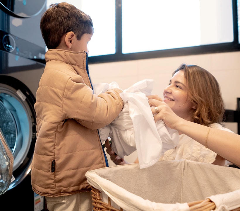 A mãe agradece ao filho por ajudar na lavandaria. Ela tem um grande sorriso na cara, observando seu filho com alegria e amor.