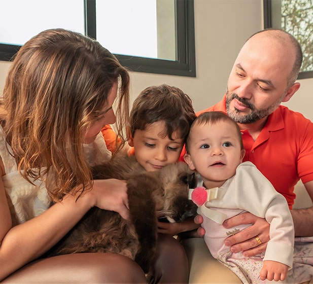 Um corte de família, cinco deles sentados de perto, incluindo um gato escuro e castanho a abraçar-se nos braços da mãe.