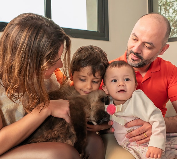 Um corte de família, cinco deles sentados de perto, incluindo um gato escuro e castanho a abraçar-se nos braços da mãe.