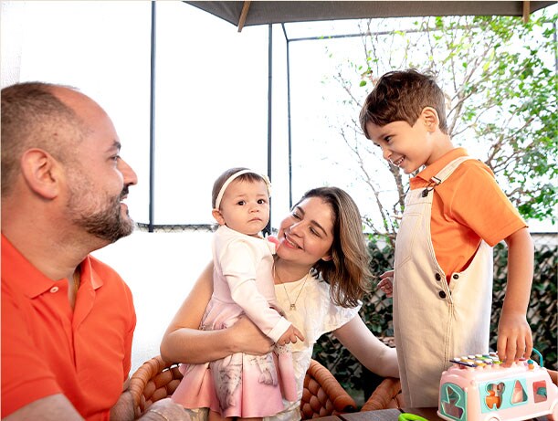 Cortado de família, sorrindo felizmente. A mãe segurava a filha nos braços, o pai e o filho também pareciam bonitos. O filho a segurar o brinquedo.