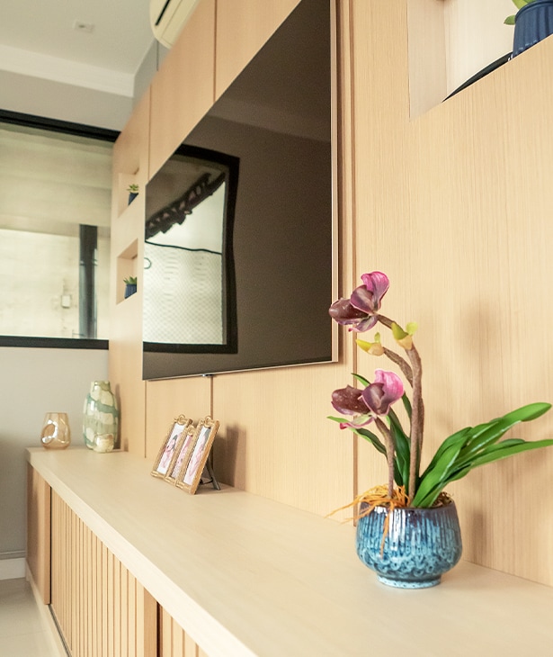 Uma bela cena interior da casa de tom beige, TV pendurado na parede. Vaso de flores e algumas fotos emmarcadas na mesa unidas à parede.