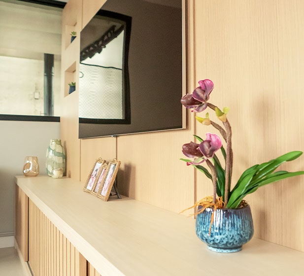 Uma bela cena interior da casa de tom beige, TV pendurado na parede. Vaso de flores e algumas fotos emmarcadas na mesa unidas à parede.