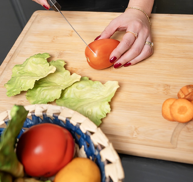 A mãe cortou um tomate vermelho. Algumas cenouras já foram cortadas, tomate e outros vegetais na tigela.