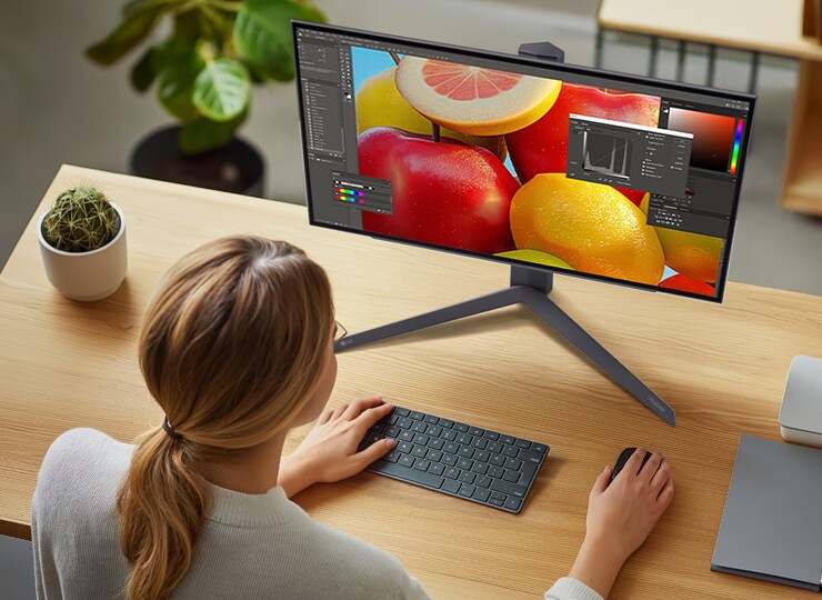 Pessoa editando uma imagem vibrante de frutas em um monitor LG, usando fones de ouvido.