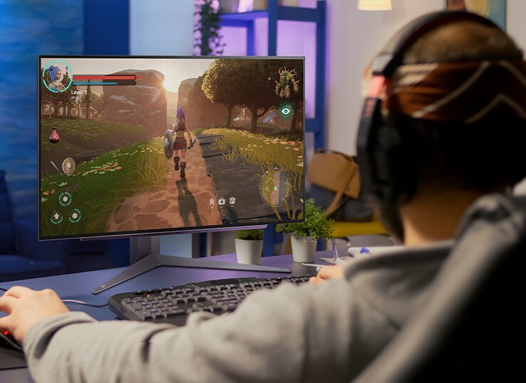 Pessoa jogando em um monitor LG com uma cena de jogo colorida em uma sala com pouca luz.