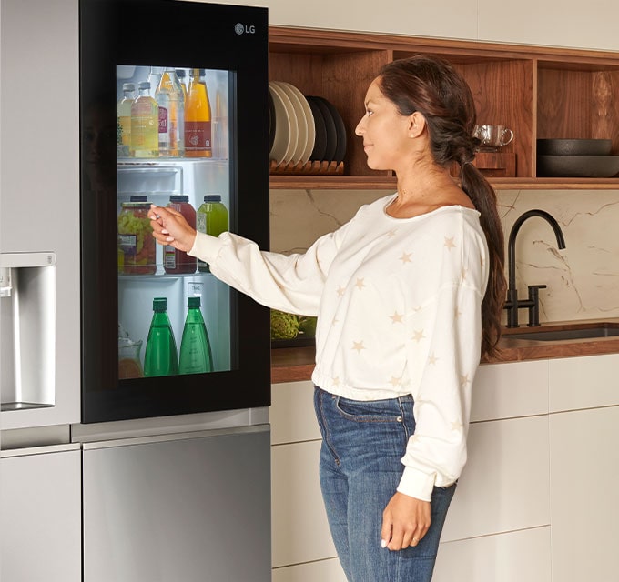 Mulher interagindo com a função InstaView Door-in-Door da LG para acessar bebidas sem abrir o refrigerador inteiro.