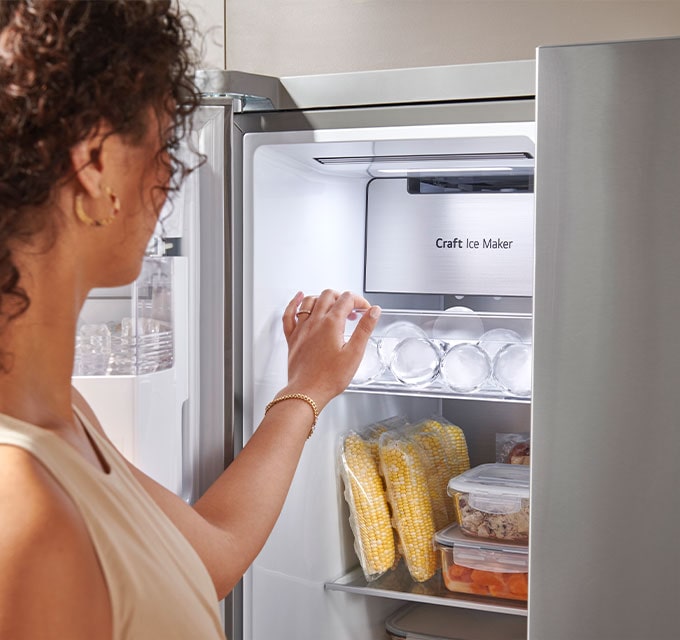 Pessoa acessando o fabricante de gelo dentro do refrigerador LG, com alimentos organizados.
