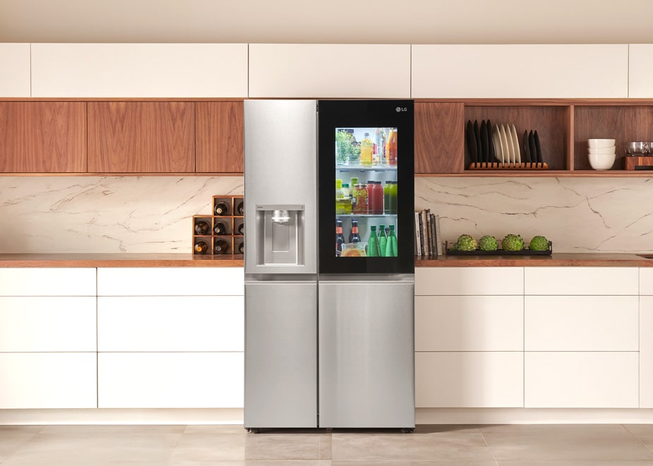 Vista frontal do refrigerador LG GC-X257CSHS em uma cozinha moderna com armários de madeira e brancos.