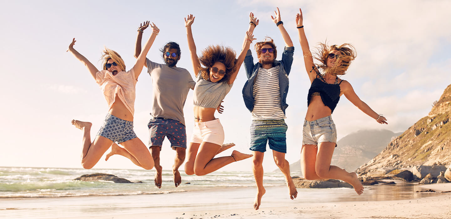 Grupo de amigos pulando na praia com o alto-falante LG XBOOM XL7S em primeiro plano.