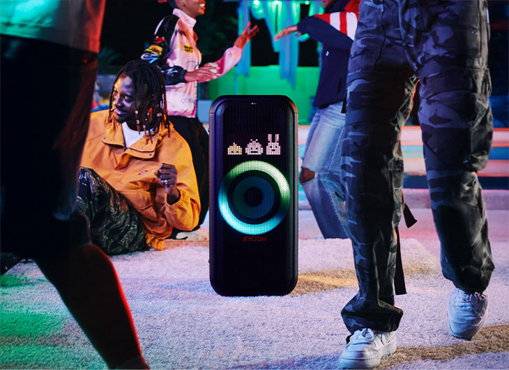 Pessoas aproveitando uma festa com a caixa de som LG XBOOM exibindo uma iluminação azul vibrante.
