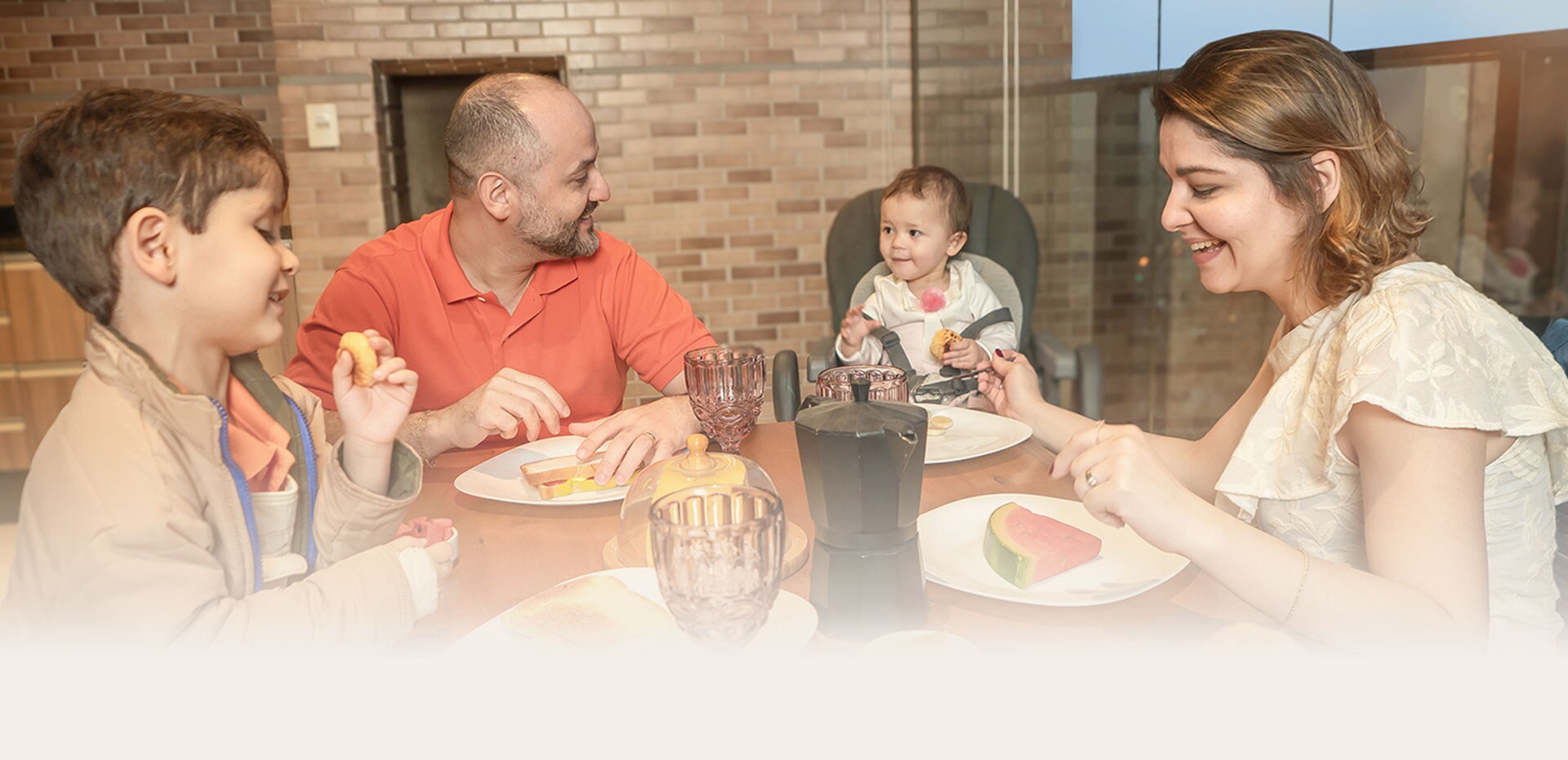 Família aproveitando uma refeição juntos na mesa de jantar, sorrindo e compartilhando tempo de qualidade.