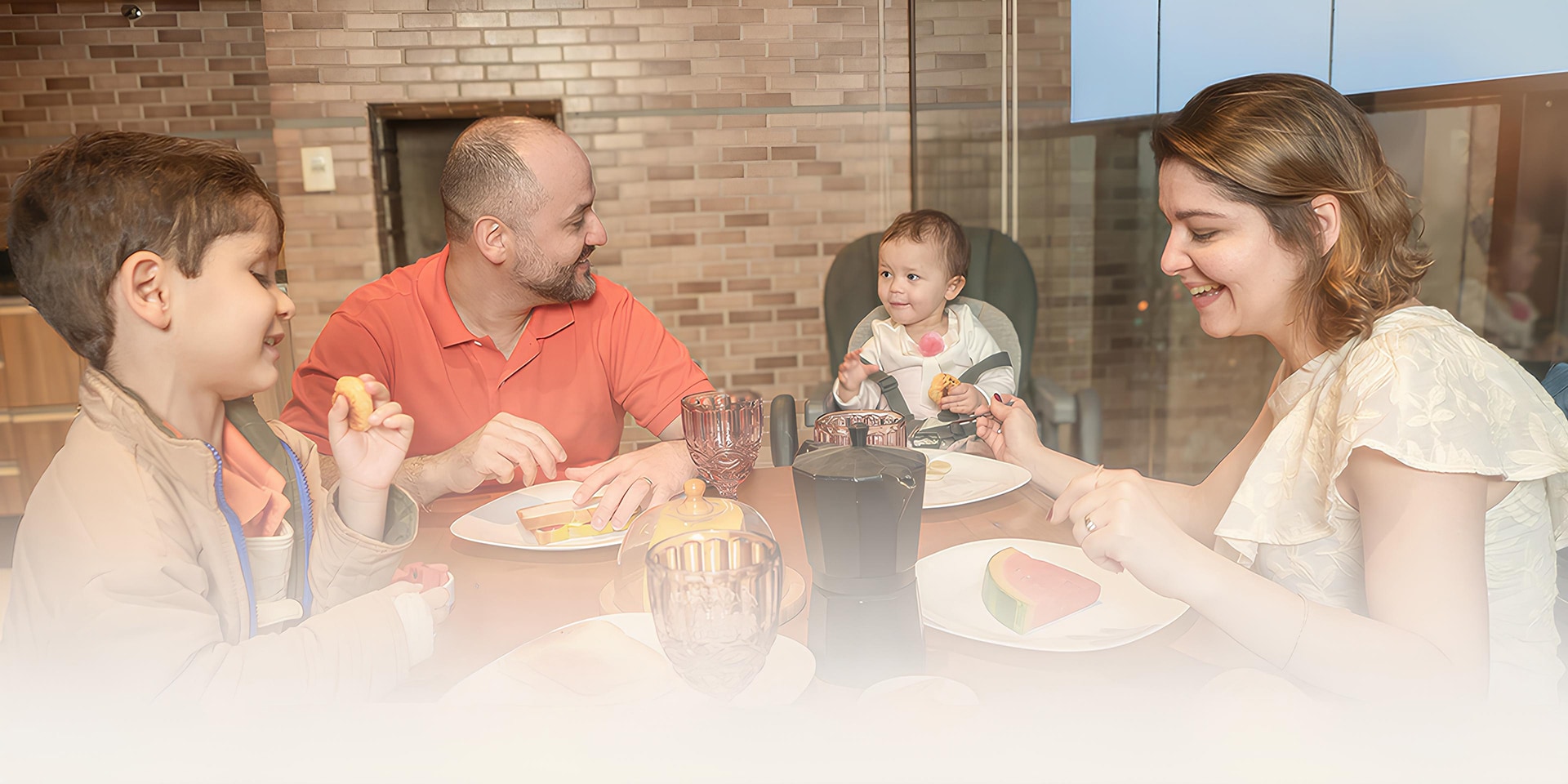 Família aproveitando uma refeição juntos na mesa de jantar, sorrindo e compartilhando tempo de qualidade.