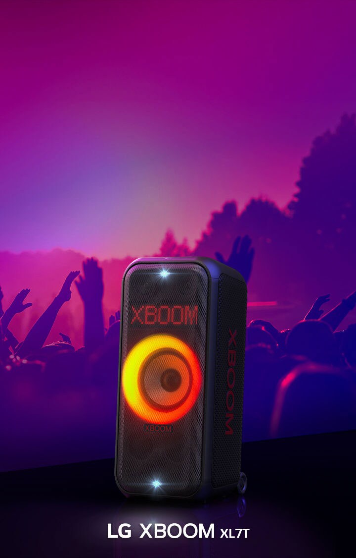 LG XBOOM XL7T posicionada no palco com uma luz gradiente vermelho-laranja ligada. Atrás do palco, pessoas curtindo a música.