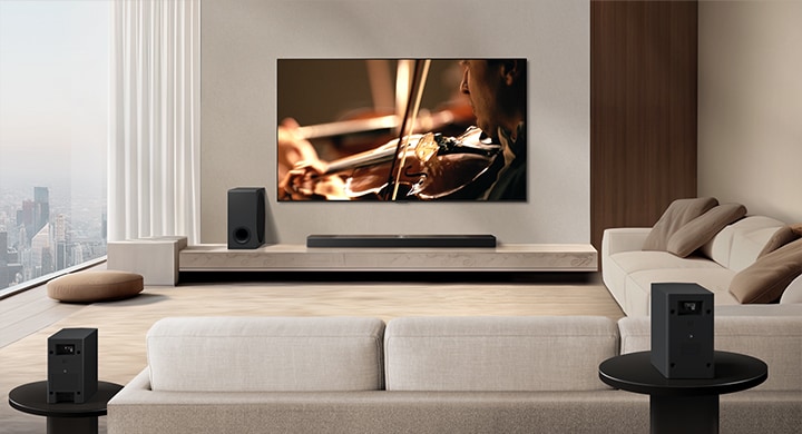 Una barra de sonido LG, un televisor LG y un subwoofer se encuentran en un moderno apartamento urbano. La barra de sonido LG emite tres ramas de ondas sonoras, formadas por gotas blancas que flotan por la parte inferior del piso. De la parte superior de la barra de sonido salen más ondas sonoras de gotitas blancas. Junto a la barra de sonido hay un subwoofer, que crea un efecto sonoro desde la parte inferior. En conjunto, crean un efecto de cúpula en toda la habitación.