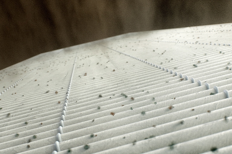 Uma infinidade de partículas de 1-3 μm aderiu à superfície do filtro MERV 13 branco.