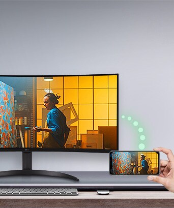 Um monitor é colocado sobre a mesa e, à direita, um telefone exibindo a mesma tela que o monitor é visível.
