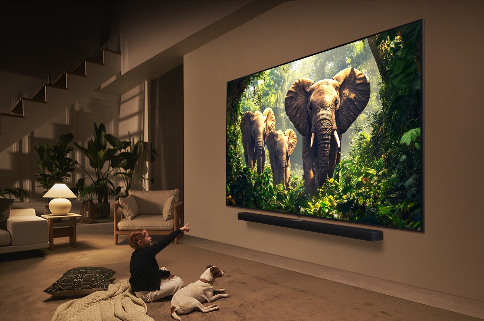 A girl and a dog are seated in front of a LG QNED TV mounted on a wall depicting three elephants walking outwards above a LG Soundbar. The title talks about how every action is more thrilling on a massive screen.