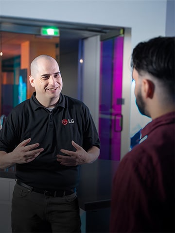 Smiling LG service representative in a black LG-branded polo shirt talking to a customer, representing LG’s friendly and knowledgeable appliance support and customer care.