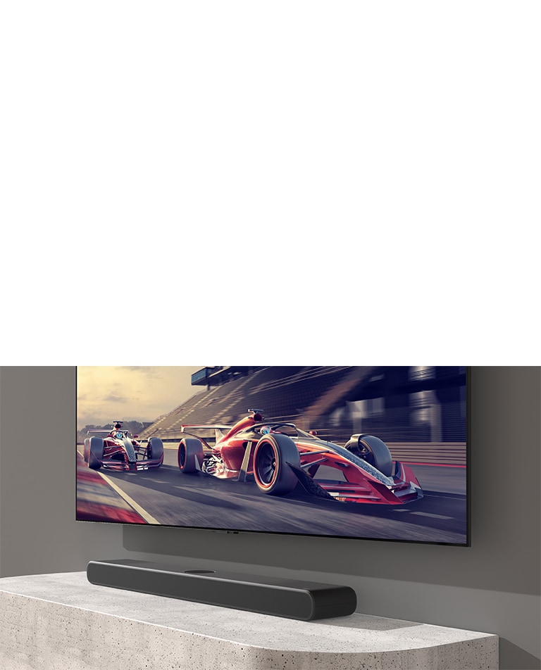 Sound bar and TV are placed on the white table and a racing scene is shown on the TV.