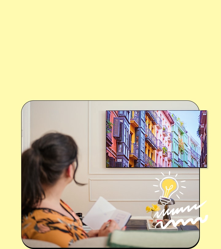 The woman is watching television with a notebook.