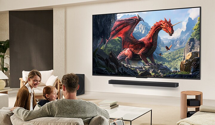 Une famille est assise sur un canapé face à un LG QNED TV monté sur un mur au-dessus d’un LG Soundbar. Une petite fille pointe du doigt un écran représentant deux dauphins.