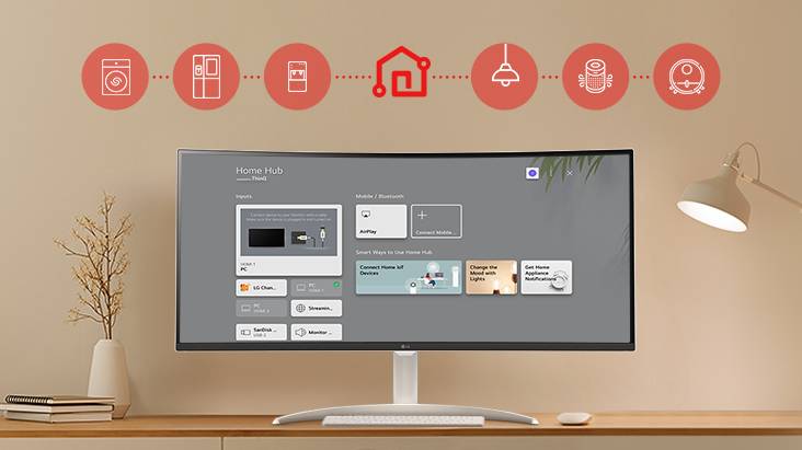 Sur l’écran du moniteur posé sur la table, le tableau de bord Home est affiché. En haut de l’image, on peut voir des icônes d’appareils électroménagers tels que des lave-linge, des réfrigérateurs, des aspirateurs, etc., qui peuvent être contrôlés via l’application LG ThinQ.
