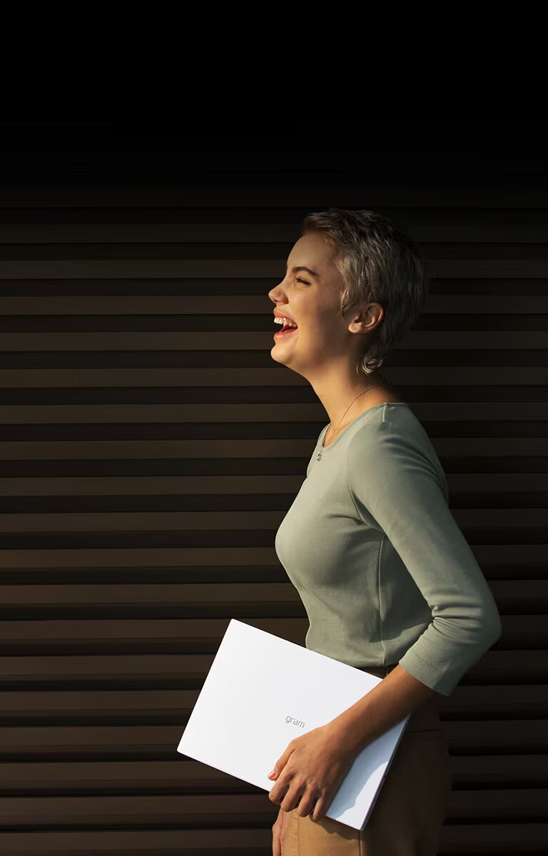 Une femme tient un LG gram et affiche un grand sourire.