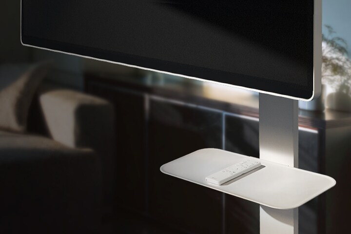 LG Smart Monitor Swing Stand Plate montrée tenant une télécommande, placée dans un salon confortable.