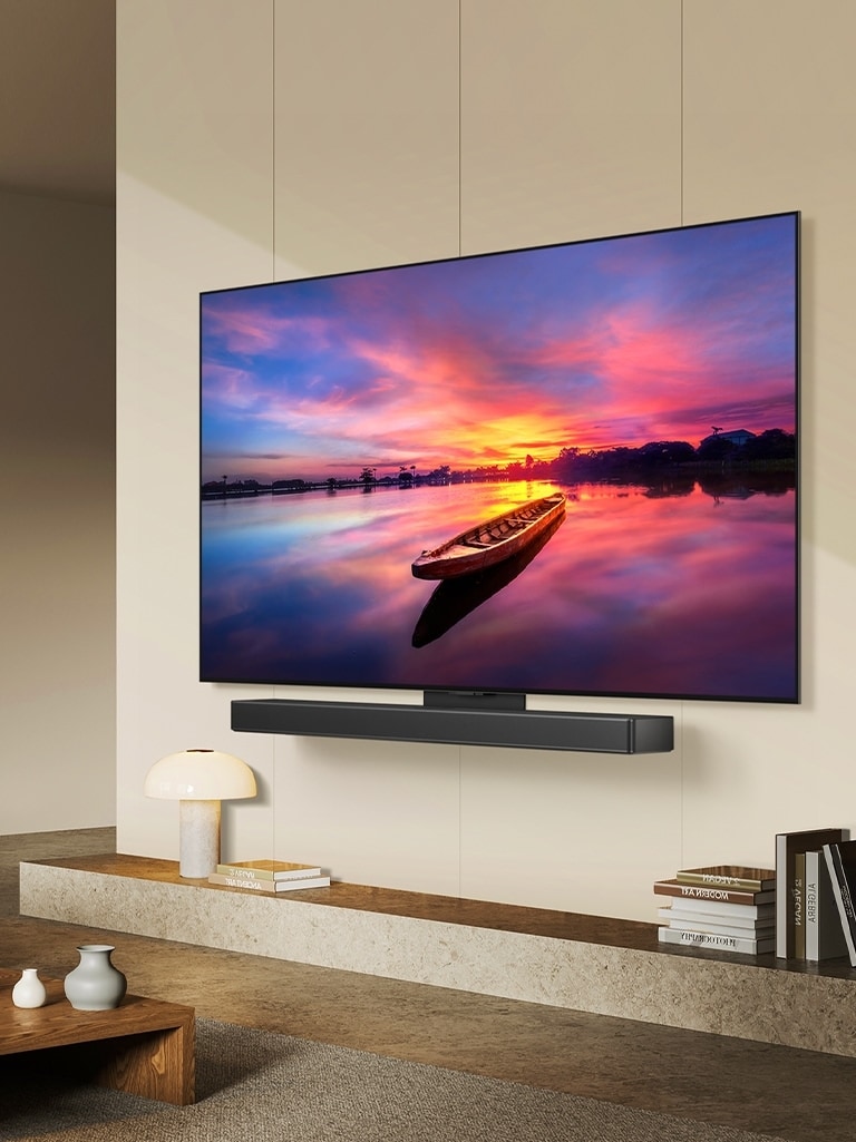 TV OLED LG, OLED C4 orienté à 45 degrés vers la gauche affichant un magnifique coucher de soleil avec un bateau sur un lac ; le téléviseur est fixé à une barre de son LG via le support Synergy dans un espace de vie minimaliste.