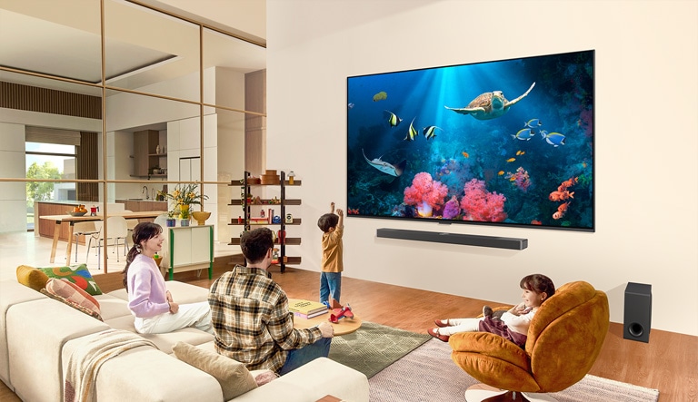 Une famille dans un salon avec un très grand téléviseur LG fixé au mur, avec une scène d’océan comprenant du corail et une tortue sur l’écran.