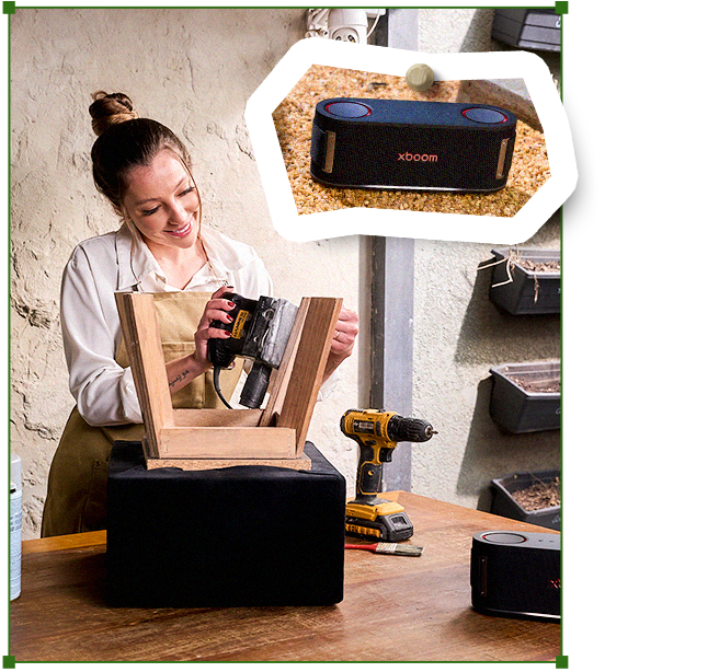 Carol reparando una silla de madera en su banco de trabajo, con un parlante LG XBOOM cerca y herramientas sobre la mesa.