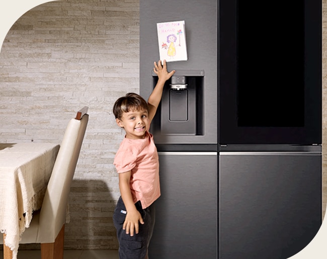 Niño colocando un dibujo de flores y pastel en la puerta del refrigerador; la madre sonríe al encontrar flores reales escondidas dentro.