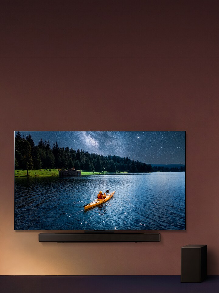 LG TV y LG Soundbar montados en la pared y un subwoofer en el suelo a la derecha. En el televisor, se muestra una persona en un kayak en un lago, y por la pared caen sombras suaves en cascada.
