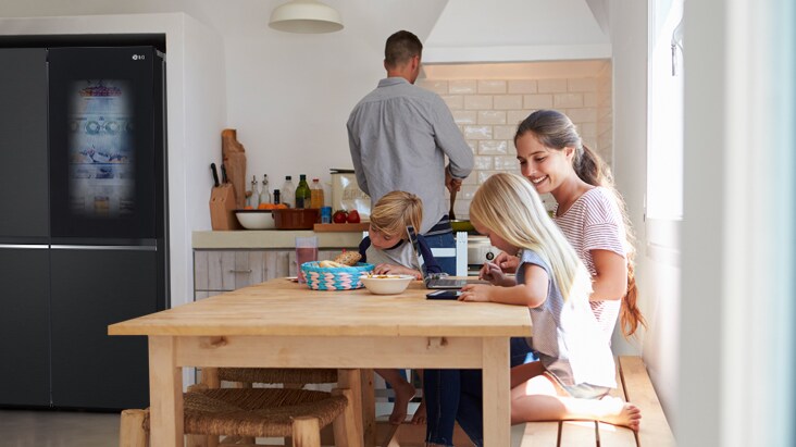 Una familia en una cocina moderna con refrigerador LG side by side a la derecha.